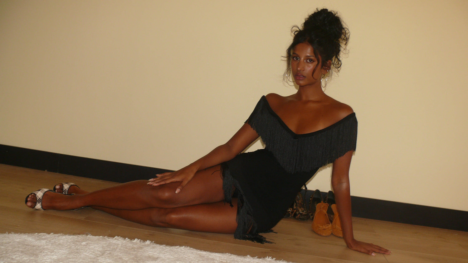 Woman in a black dress sitting on the floor against a beige wall.